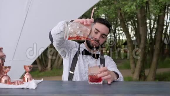 酒吧柜台上的酒吧服务员用冰块在果汁中加入酒精准备用冰块冷却鸡尾酒视频的预览图