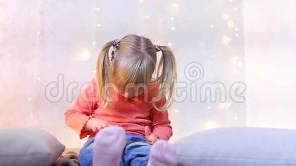 小女孩坐在房间的地板上装饰着圣诞节的装饰在电话里玩游戏视频的预览图