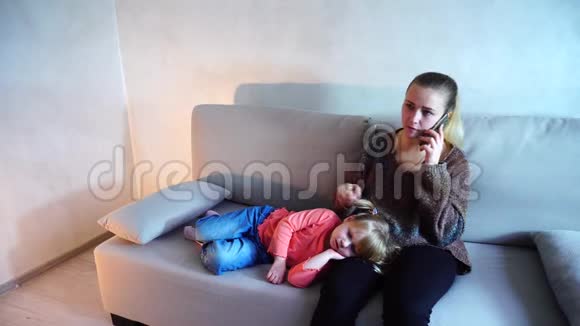 年轻的母亲坐在客厅的沙发上小女儿跪在地上视频的预览图
