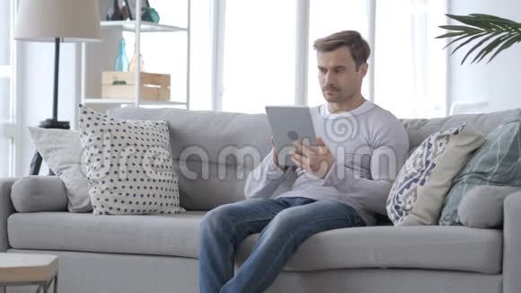 坐在沙发上用平板电脑的严肃男人视频的预览图
