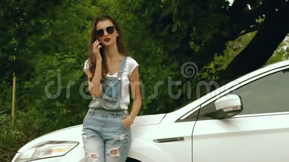 一位戴着明亮太阳镜的漂亮女孩在汽车旁用电话说视频的预览图