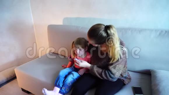 金发的年轻母亲坐在沙发上擦鼻涕的小女儿视频的预览图