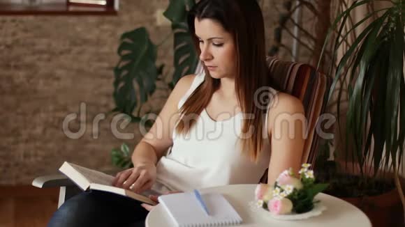 年轻漂亮的女人看书和做笔记坐在椅子上看书的女人视频的预览图