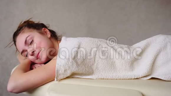 美丽的女人的肖像按摩后放松低头看躺在沙发上毛巾下明亮的医疗视频的预览图