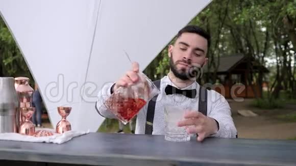 酒吧服务员将冰镇的酒倒入装有冰块的玻璃杯中酒吧服务员在酒吧柜台准备冷却鸡尾酒夏季咖啡厅视频的预览图