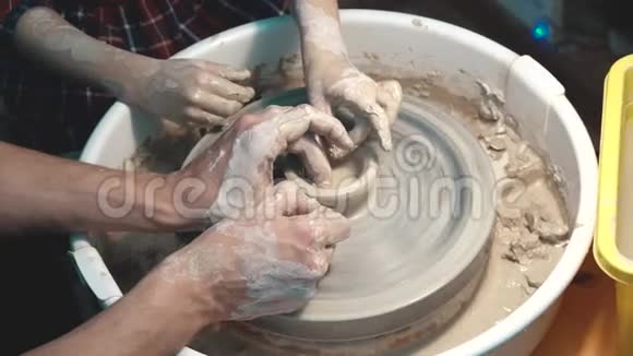 陶工教孩子做陶工轮子成人和儿童双手特写视频的预览图