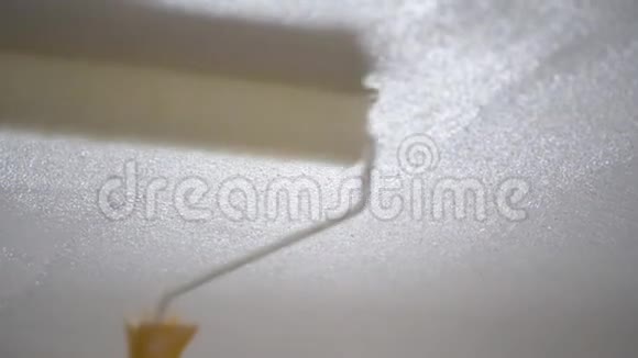 一个女人用滚筒把米色的墙涂上白色的油漆视频的预览图