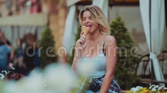 一个穿着休闲装的金发女郎站在咖啡馆外骑着自行车开心地吃着冰淇淋视频的预览图