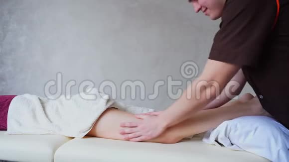 专业男性按摩师手工制作抗纤维素足底按摩躺在明亮沙发上的女性患者视频的预览图