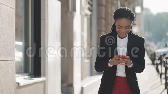 漂亮的女商人使用智能手机在商业中心附近的街道上行走黑色时尚可怕的家伙视频的预览图