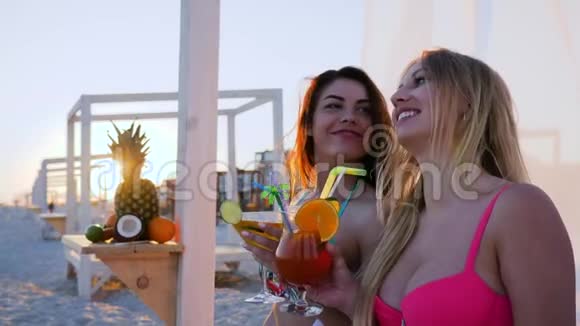 女朋友在手机上拍照姐妹在日落时在海边喝鸡尾酒视频的预览图