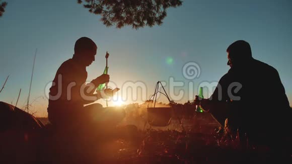 两名游客坐在篝火旁的生活方式让智能手机派对在大自然中露营剪影阳光日落视频的预览图