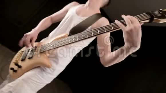 年轻的男音乐家穿着白色的衣服黑色背景上有一把米色的低音吉他低音吉他演奏者演奏音乐视频的预览图