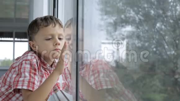 伤心的小男孩白天站在家窗户附近视频的预览图