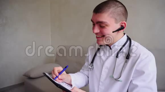 现代男性医生通过蓝牙与病人交谈并写信给接待处白天坐在诊所的办公室视频的预览图