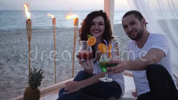 带着鸡尾酒的朋友在海滩上度过一个异国情调的假期在平房浪漫的旅行背景热带水果火视频的预览图