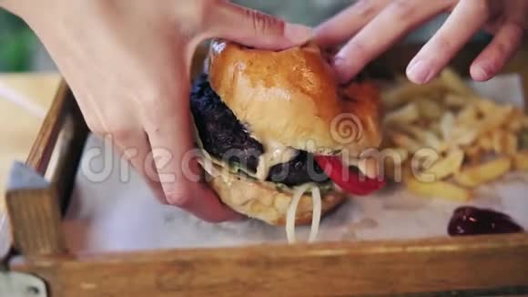 女性的手从一个木制托盘里拿着美味的大汉堡准备吃它慢镜头视频的预览图