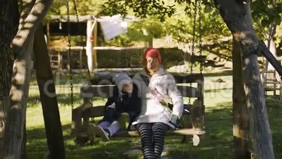 早上祖母和孩子骑在公园户外的木秋千上视频的预览图
