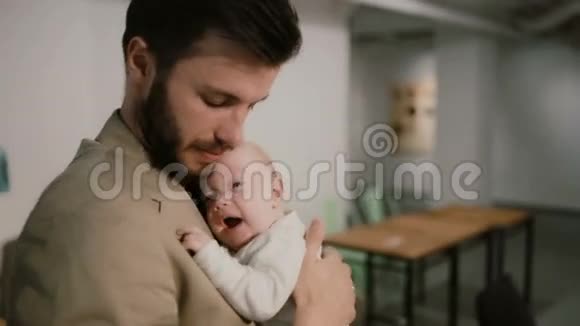 一个年轻人抱着一个婴儿在他的手臂上说话亲吻他的脸颊他的背景视频的预览图