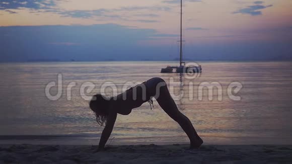 年轻女性在日落时在海滩上锻炼瑜伽做姿势狗眼镜蛇慢动作1920x1080视频的预览图