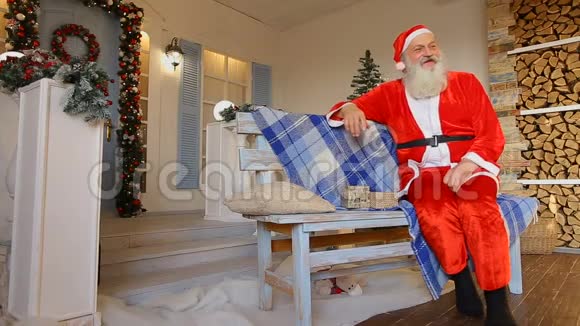 圣诞老人讲述了一个迷人的故事坐在装饰圣诞节的房子的院子里的长凳上视频的预览图