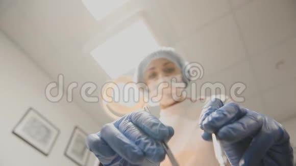 年轻的女牙医斜靠在病人身上把灯打开用戴着医用面罩的工具看着摄像机视频的预览图