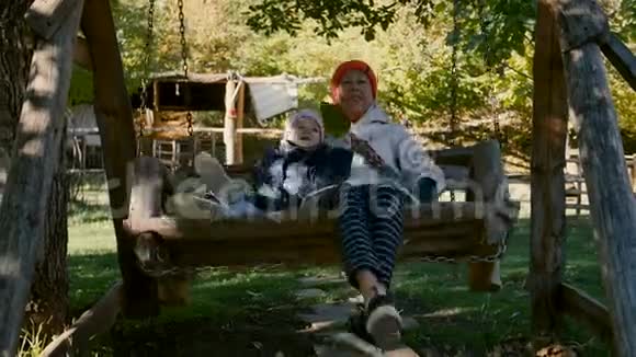 早上祖母和孩子骑在公园户外的木秋千上视频的预览图