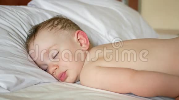 婴儿睡在一张没有衬衫的白色床上有点出汗的头发特写视频的预览图