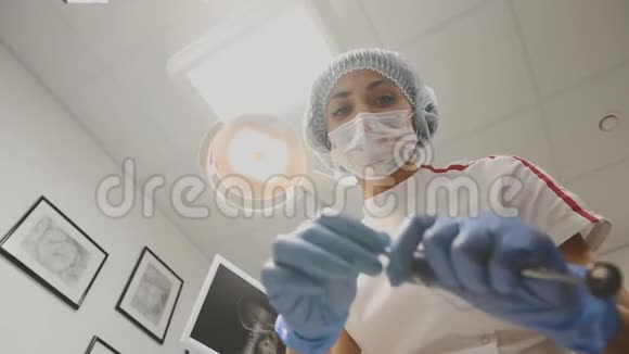 年轻的女牙医斜靠在病人身上把灯打开用戴着医用面罩的工具看着摄像机视频的预览图