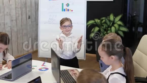 一位靠近挂图的儿童商人向同事们展示了一个项目视频的预览图