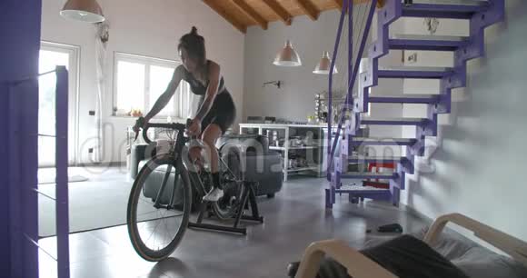 年轻的纹身骑自行车的妇女骑自行车在家里健身运动锻炼客厅家政培训4公里视频的预览图