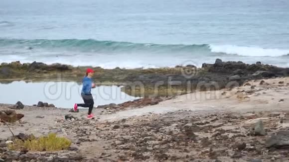 女人沿着海洋的石岸奔跑健康的积极生活方式慢动作视频的预览图