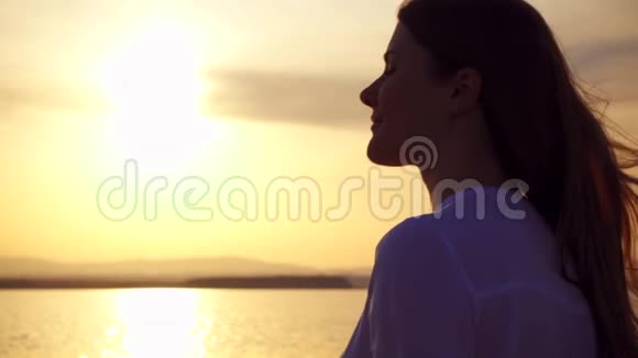 在湖上日落时微笑的年轻女子的剪影女性在黄金时刻缓慢运动视频的预览图