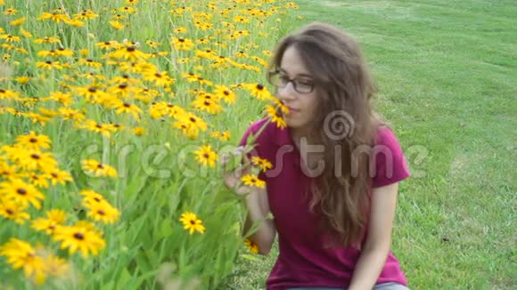 可爱的年轻女子闻着公园花坛上的黄花视频的预览图