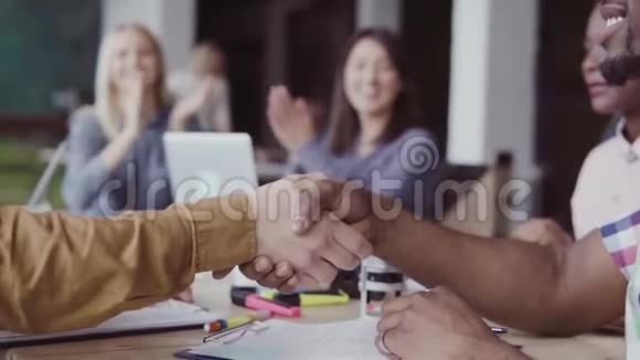 两个伙伴非洲和高加索商人握手一群人在现代办公室的背景上鼓掌视频的预览图