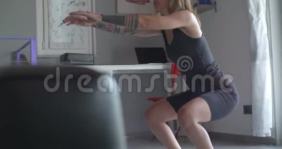 年轻的纹身妇女在家庭健身运动锻炼中做深蹲运动客厅家政培训4公里视频的预览图