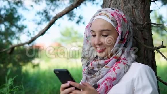 一位女士戴着头巾在公园里和朋友用智能手机聊天视频的预览图