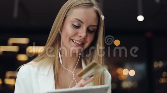 微笑的年轻女性从金色信用卡上获取了一个与平板电脑一起工作的数据视频的预览图