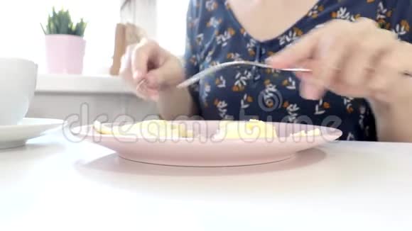 女人坐在桌子旁吃着一个带着一个民间和一把刀的小面包在家里或家里喝咖啡或茶视频的预览图