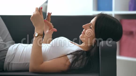 沙发上躺着平板电脑的快乐年轻女子视频的预览图