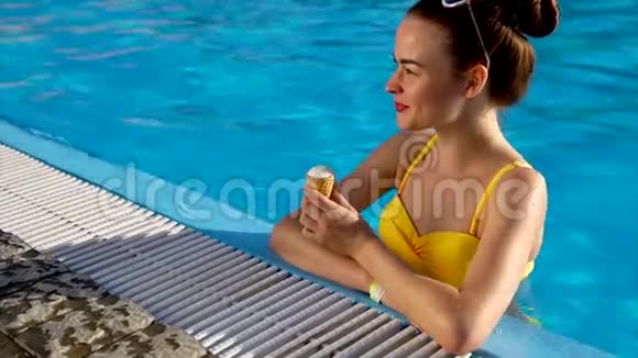美丽的年轻女子穿着泳装站在游泳池里吃冰淇淋视频的预览图
