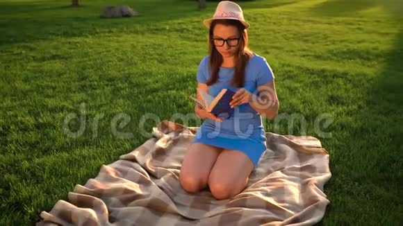戴眼镜的女孩在日落时坐在公园的毯子上看书视频的预览图