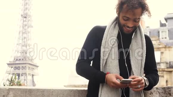 穆拉托男性通过智能手机与朋友在埃菲尔铁塔附近的耳机聊天视频的预览图