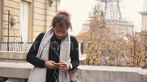 穆拉托家伙享受智能手机和耳机与埃菲尔铁塔的背景缓慢运动视频的预览图