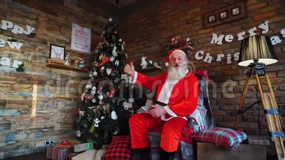快乐的圣诞老人在节日装饰的房间里表现出快乐并竖起大拇指坐在大扶手椅上视频的预览图