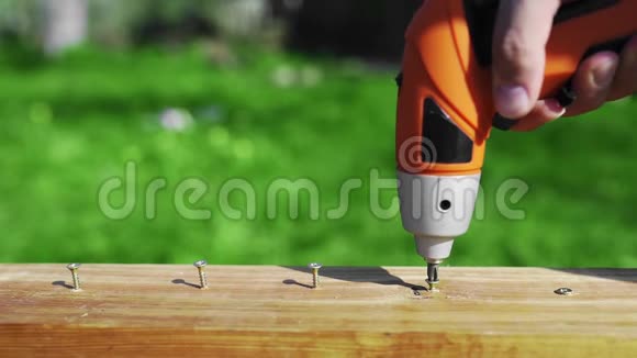 男士使用电动工具将螺丝拧到未涂漆的木块上在室外使用螺丝刀视频的预览图