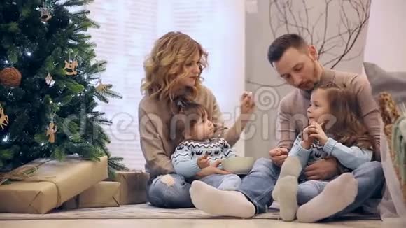 圣诞快乐一家人穿着毛衣爸爸妈妈和两个女儿坐在树下笑着互相买东西视频的预览图