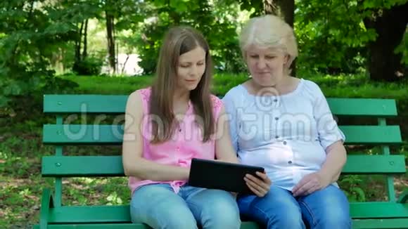 老年妇女和年轻妇女坐在公园的长凳上使用平板电脑成年母亲和女儿视频的预览图