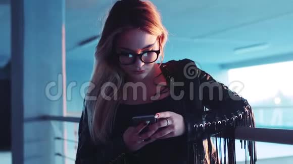 穿着黑色波西米亚风格皮夹克的金发美女用手机上网视频的预览图