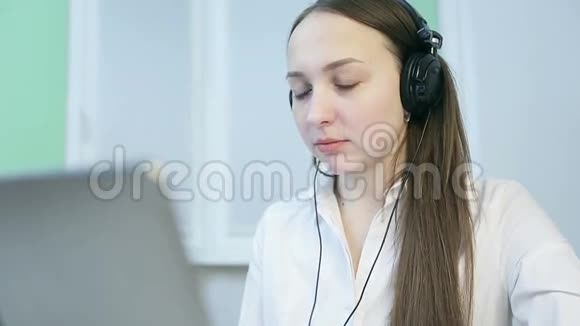戴着耳机的漂亮女孩在她的笔记本电脑上工作视频的预览图